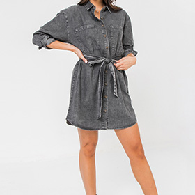 This denim dress features a shirt collar, full front button and self sash tie.